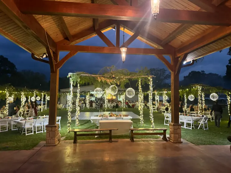 Timber pavilion at night with a lit evergreen garland arch and banqueting tables beneath it.