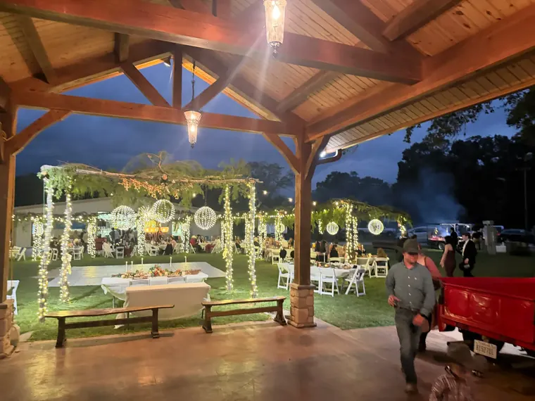 Timber pavilion at night with lit garland arch, tables and warm lighting on the roof structure.