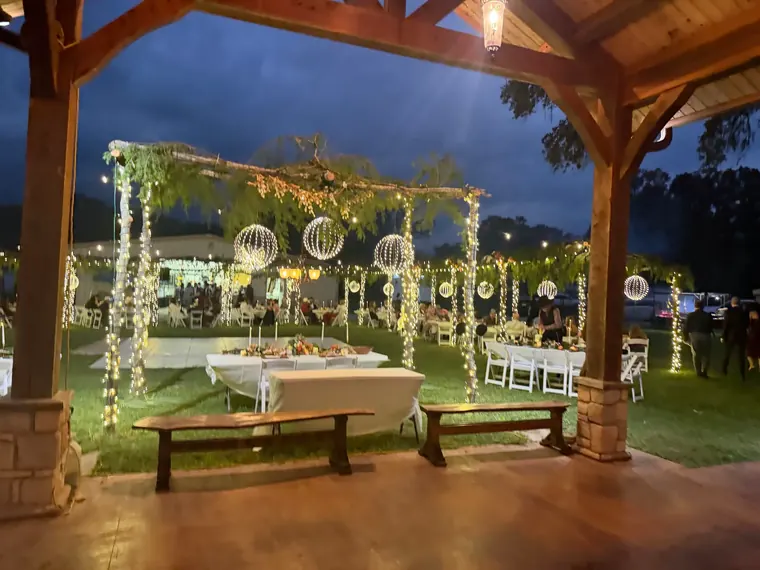 Pavilion at night with lit arch, garland on the columns and tables set for dinner.