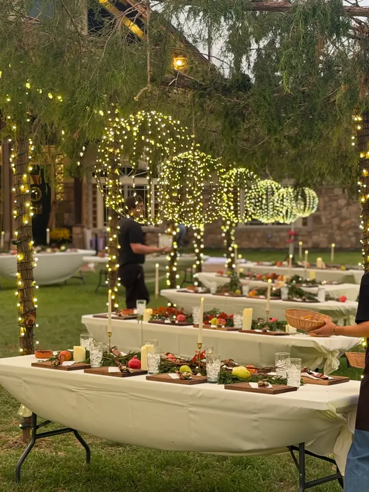 Close view of a banqueting table under wrapped trees with hanging light spheres overhead.