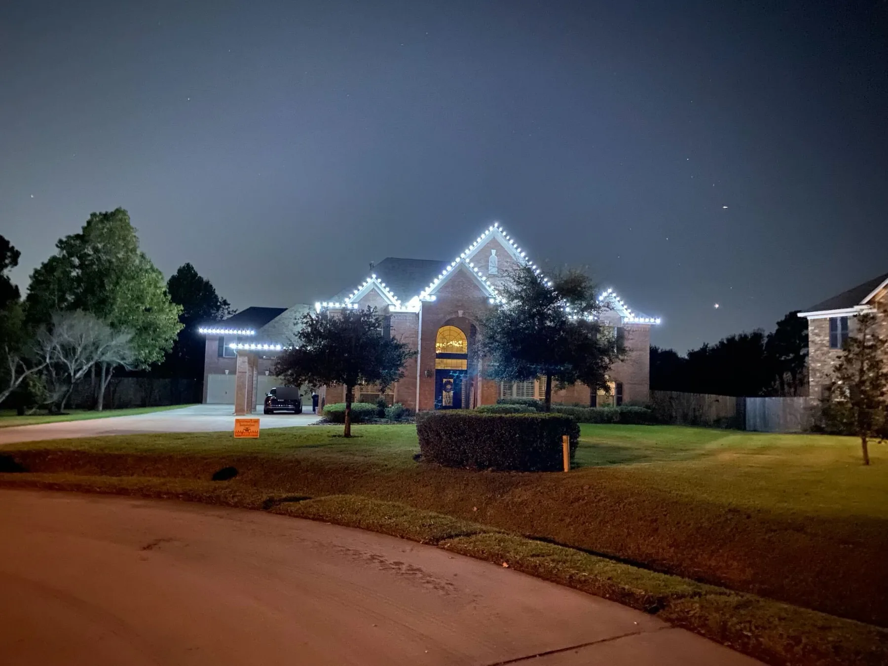 Two-story brick home at night with crisp cool-white lights outlining every gable and the garage roofline. Representative of installs like those near Pinehurst.