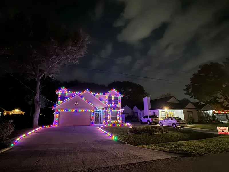 Two-story home at night with multicolor C9 lights on every roofline, around the windows and down both sides of the driveway.