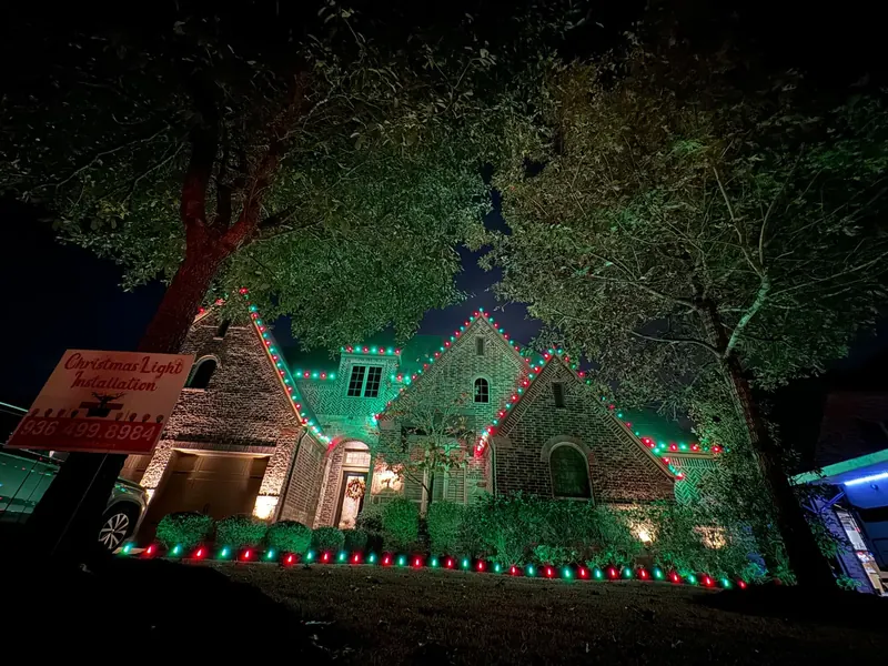 Brick Tudor-style home with three steep gables outlined in red and green lights and a row of red and green C9 bulbs along the front beds.