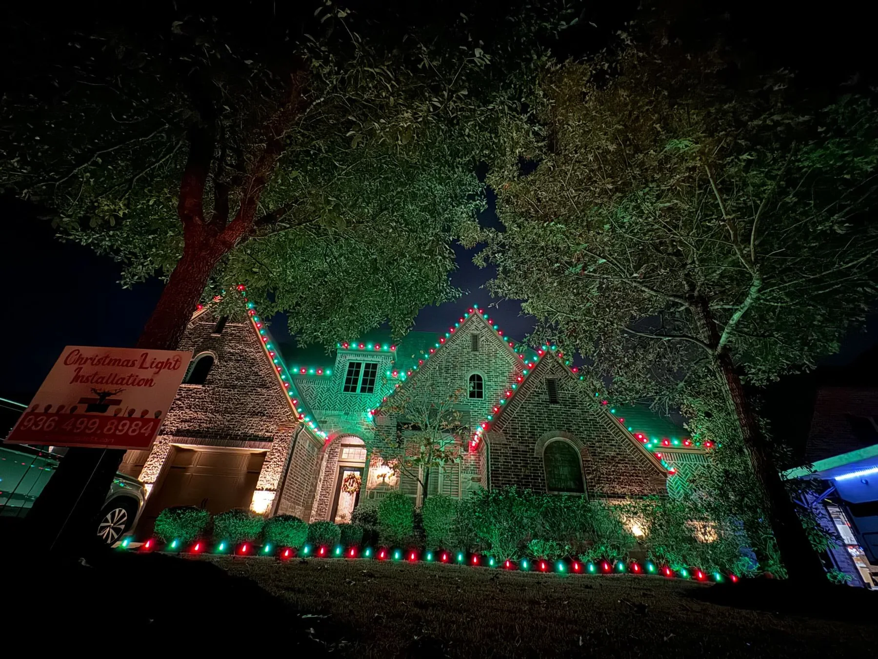 Brick Tudor-style home with three steep gables outlined in red and green lights and a row of red and green C9 bulbs along the front beds. Representative of installs like those near Tomball.