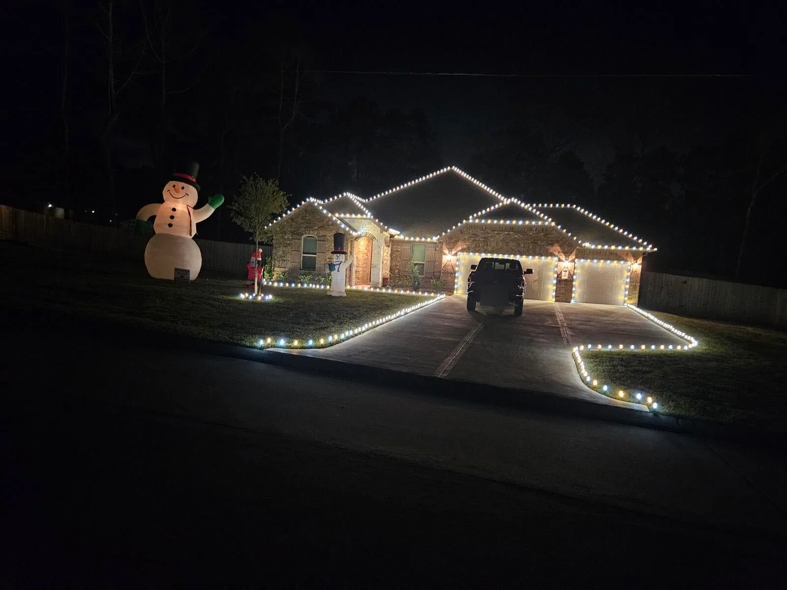 Brick ranch home on a dark street with warm-white rooflines, garage doors outlined and a driveway edged in C9 lights. Representative of installs like those near Spring.