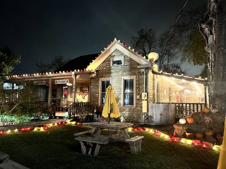 Historic wood-sided storefront at night with red and white C9 lights along the roofline and ground, and a lit patio.
