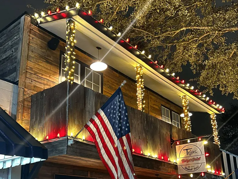 Restaurant building with red and warm-white lights on the roofline, lit wrapped posts and a flag at the entrance.