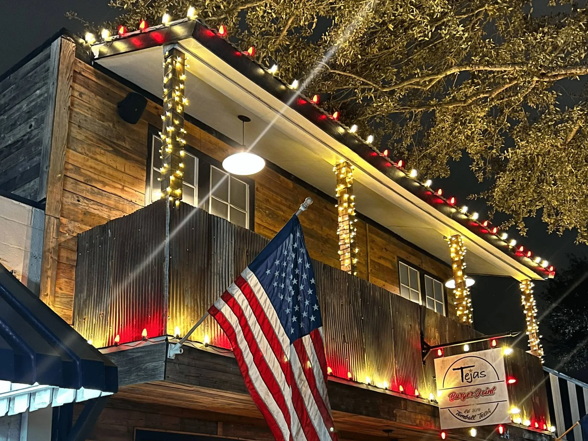 Tomball restaurant porch at night with red roofline lighting and warm-white wrapped timber columns.