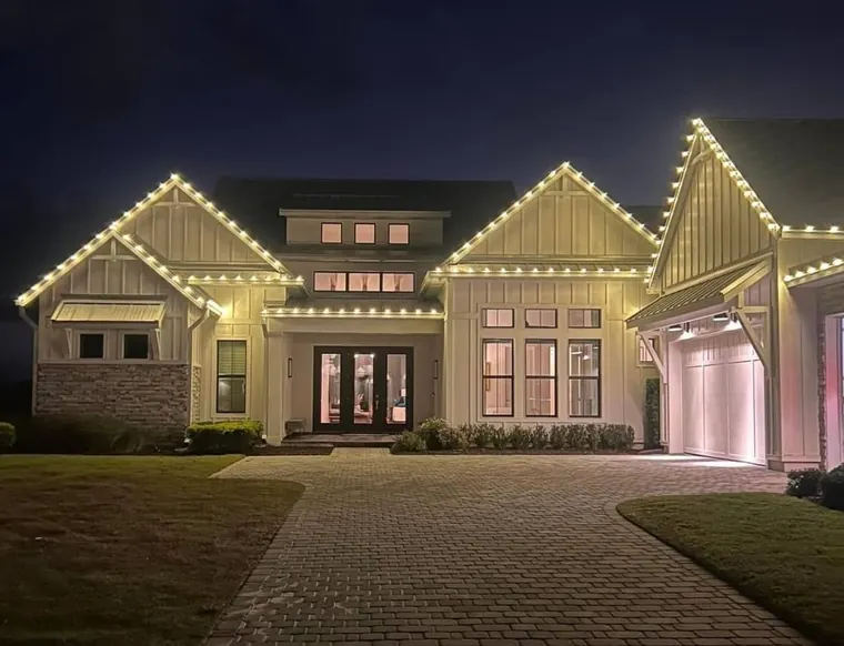 Modern farmhouse with a paver driveway and warm-white lights outlining each gable and the garage.